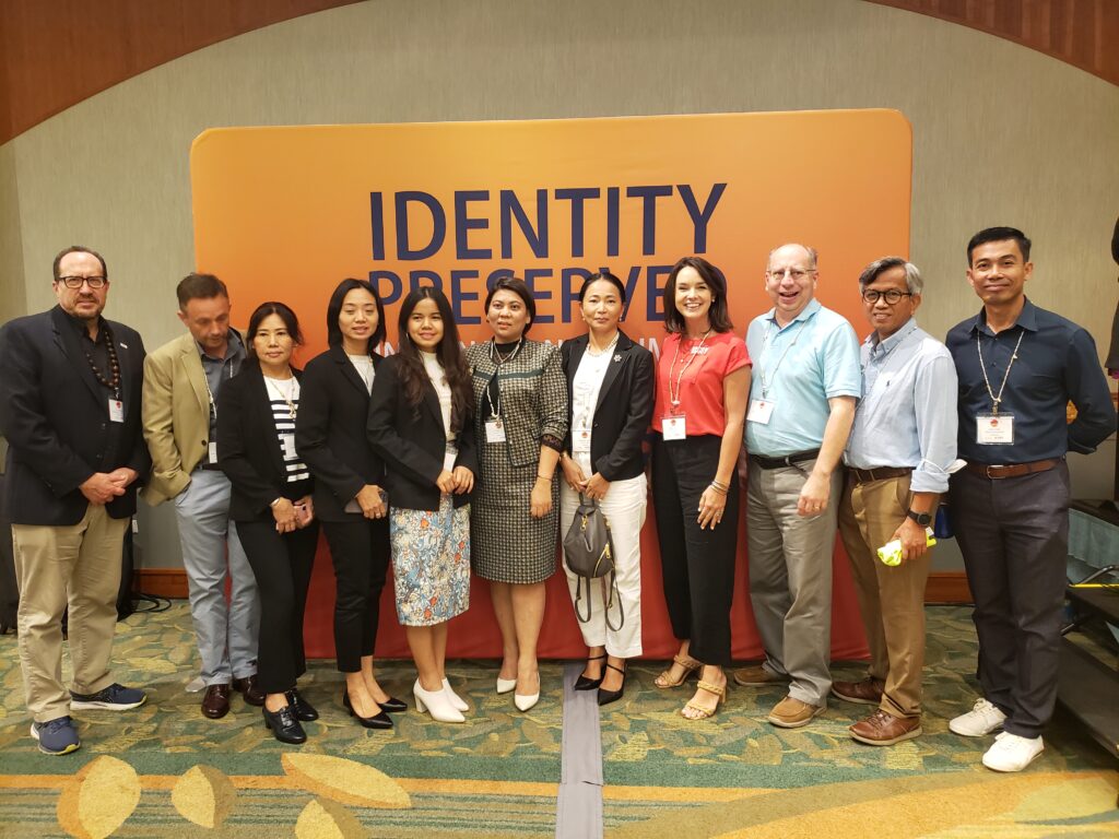 Eleven individuals standing in front of an event banner that says "Identity Preserved International Summit."