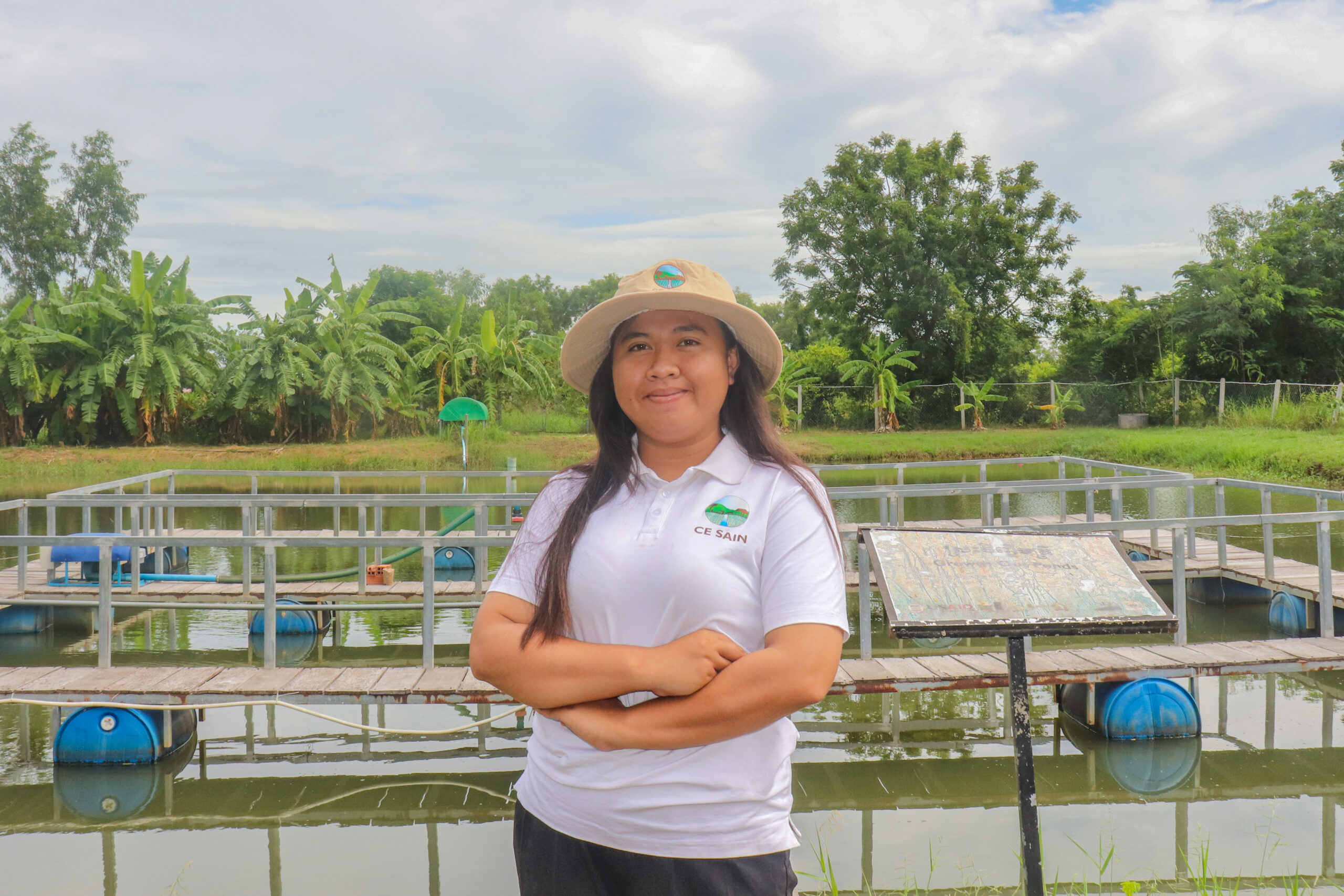 A person standing in front of a fish farm pond in Cambodia with a shirt bearing CE-SAIN.