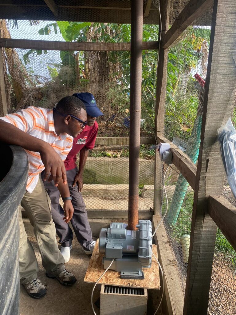 Two men standing on the left looking at a regenerative air blower used for aeration for fish ponds.