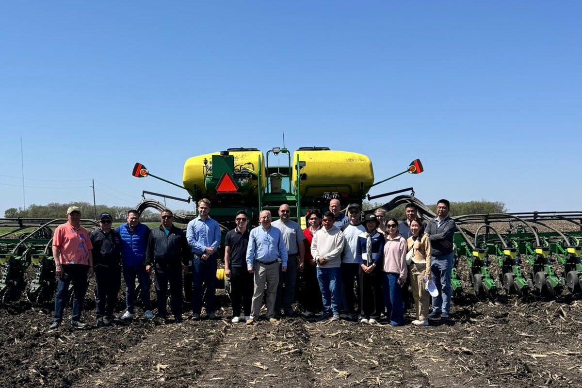 A group of men and women stand in a soybean field, posed in front of an agricultural planter.