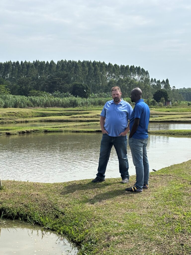 Two men speaking to each other as they stand in front of a lake.
