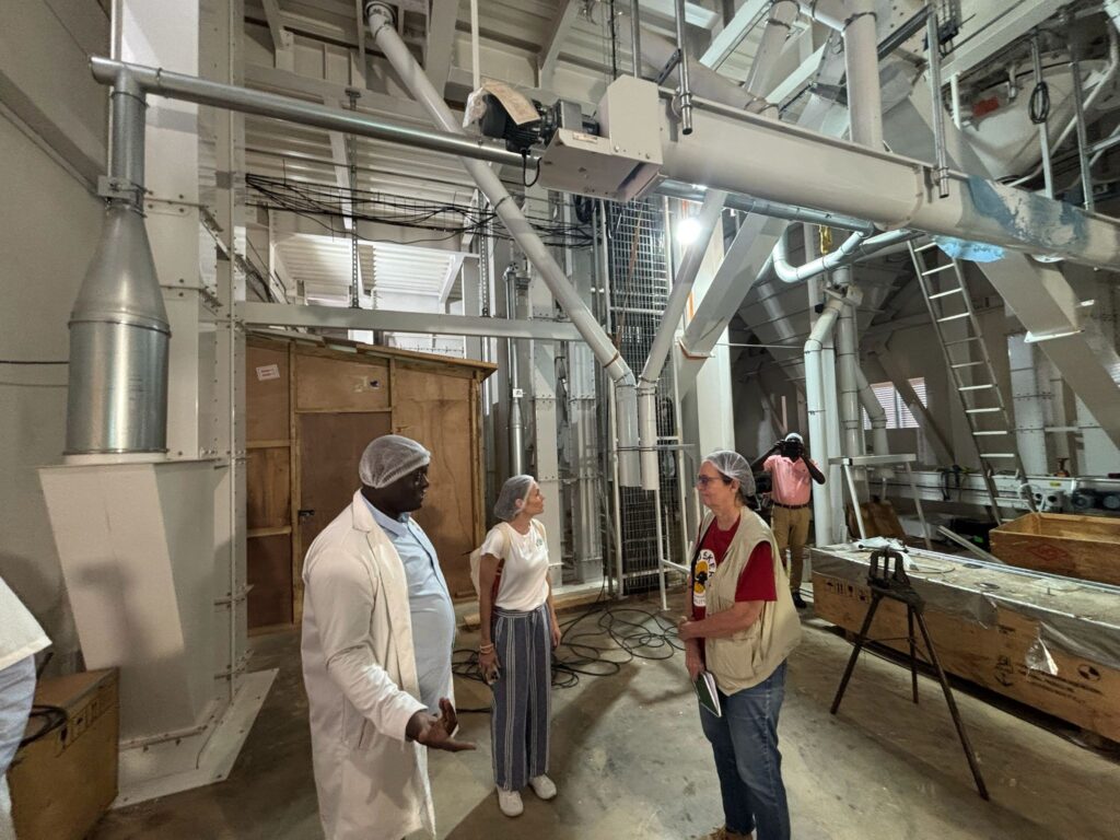 Two women speak to a man in a building where they are wearing person protective equipment.