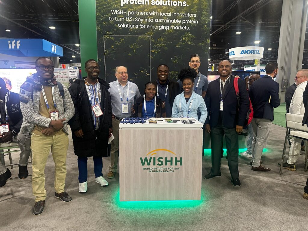 A group of people stand together for a group photo with a counter displaying the WISHH logo splits them down the middle.