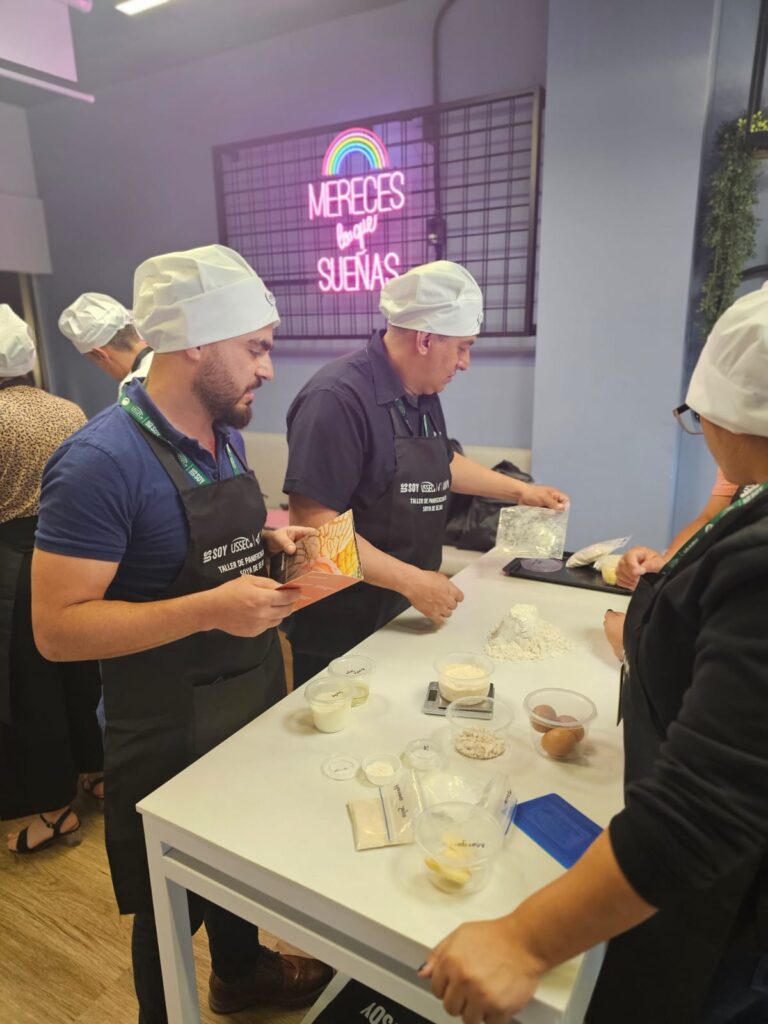 3 people stand together around a table with baking ingredients.