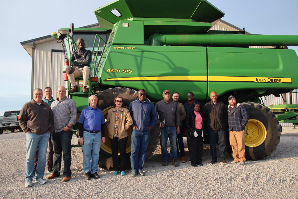 A group of people posing for a photo in front of a piece of farm equipment.