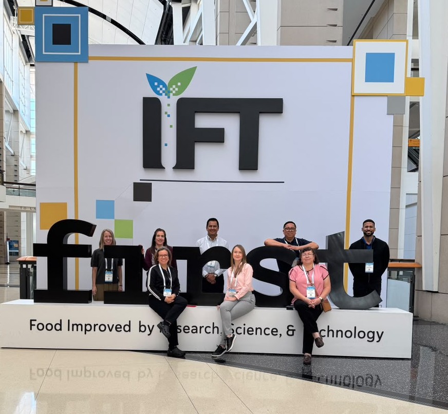 A group people pose in front of an IFT FIRST signage display.